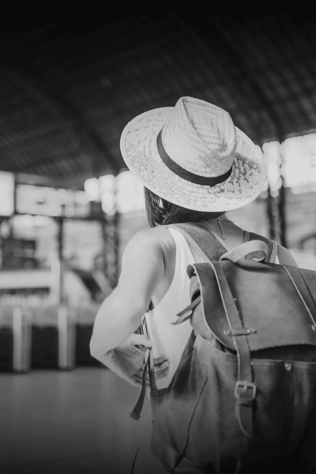 Mujer con sombrero y mochila, de espaldas, en el hall de una estación de trenes.