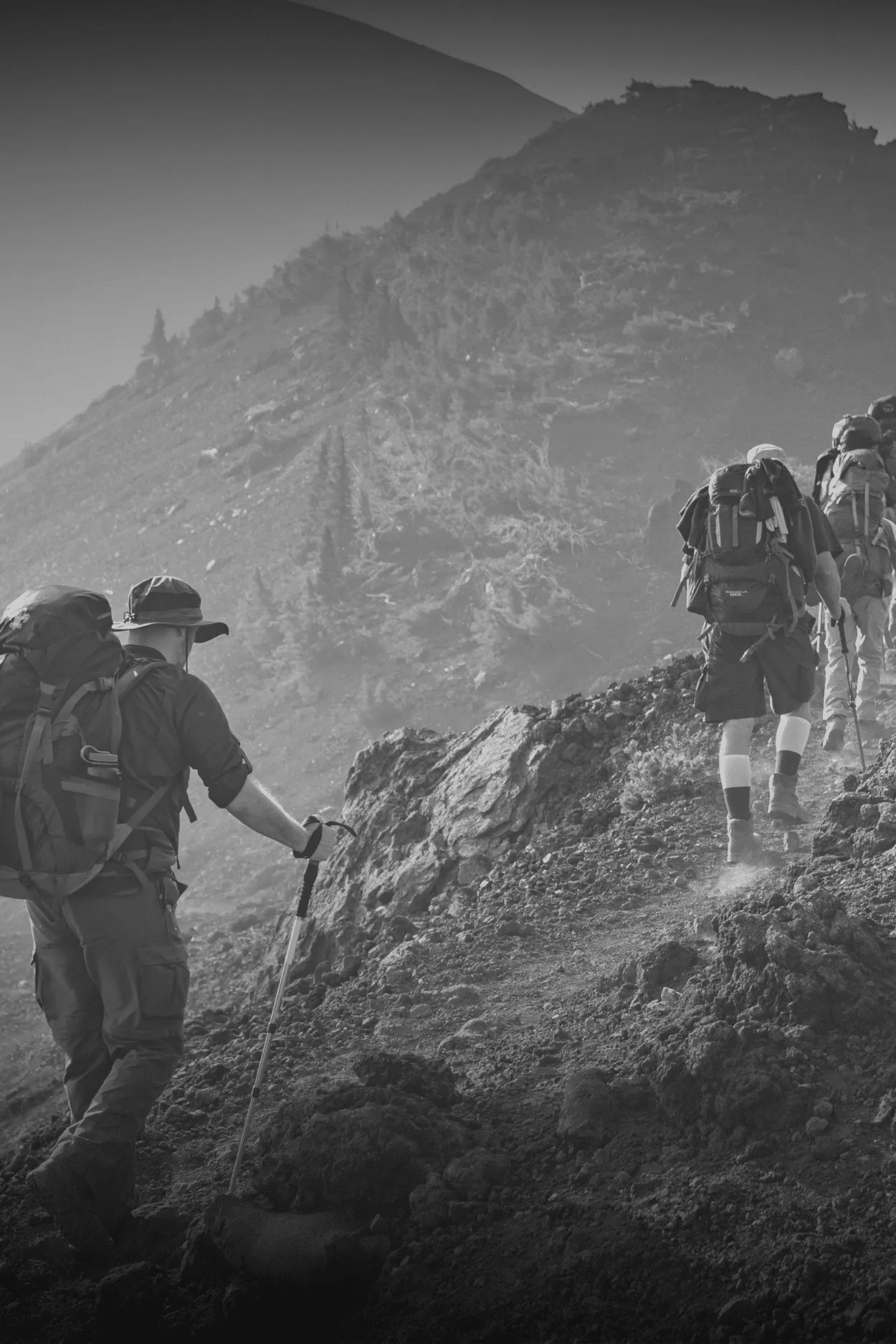 Excursionistas con mochila suben una ladera rocosa.