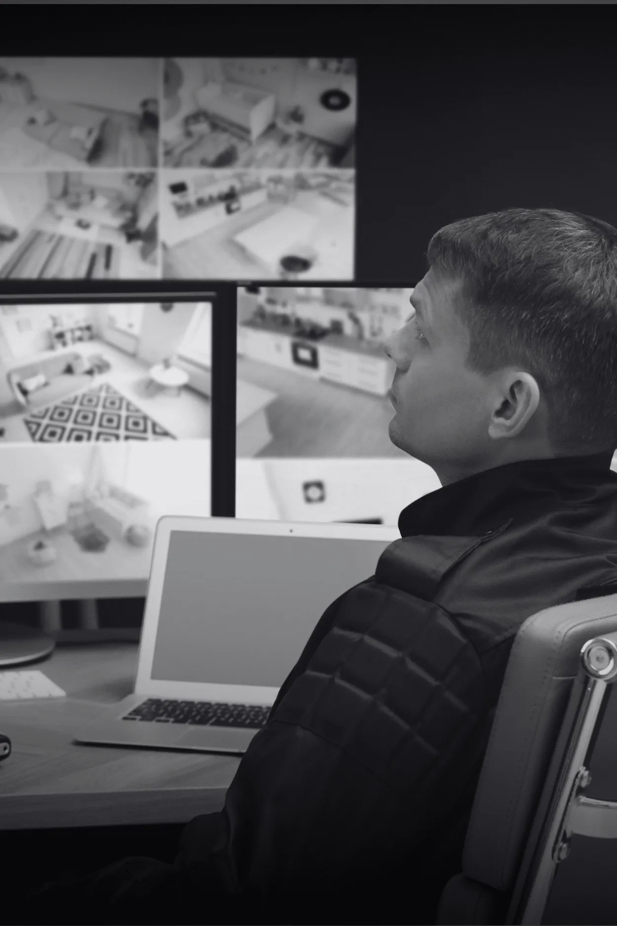 Hombre de perfil observa un muro de monitores con cámaras de interior.