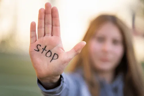 Una joven levanta la palma de la mano, donde está escrito stop, con el rostro desenfocado.