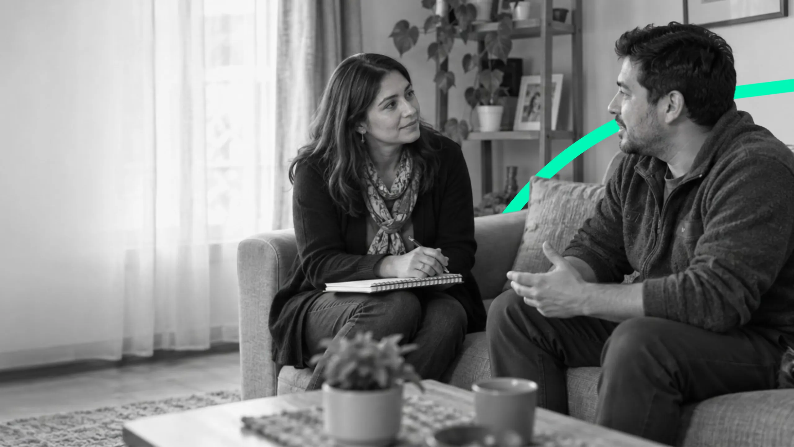 Una mujer con cuaderno y un hombre conversan sentados en un sofá.