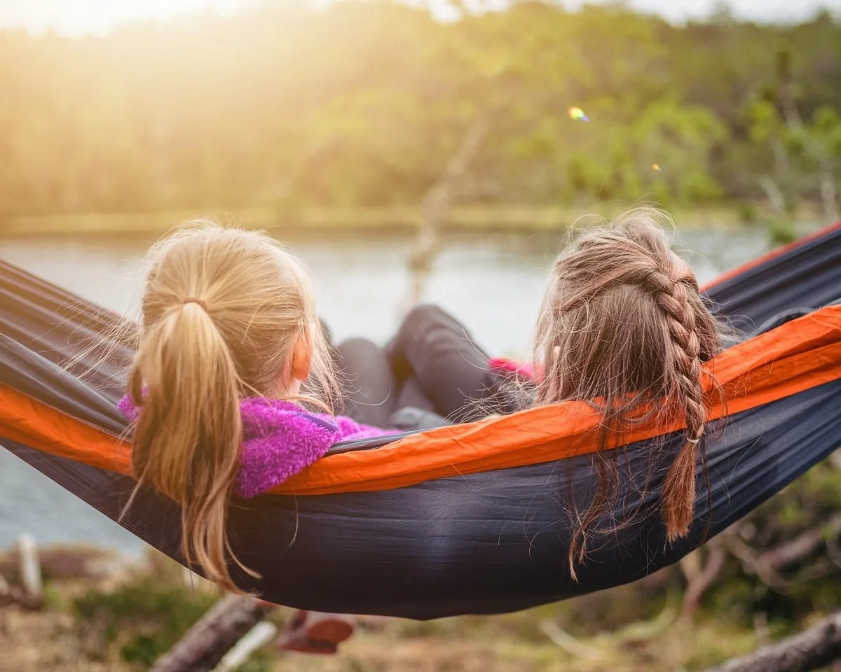 Dos chicas en hamaca viendo un lago.