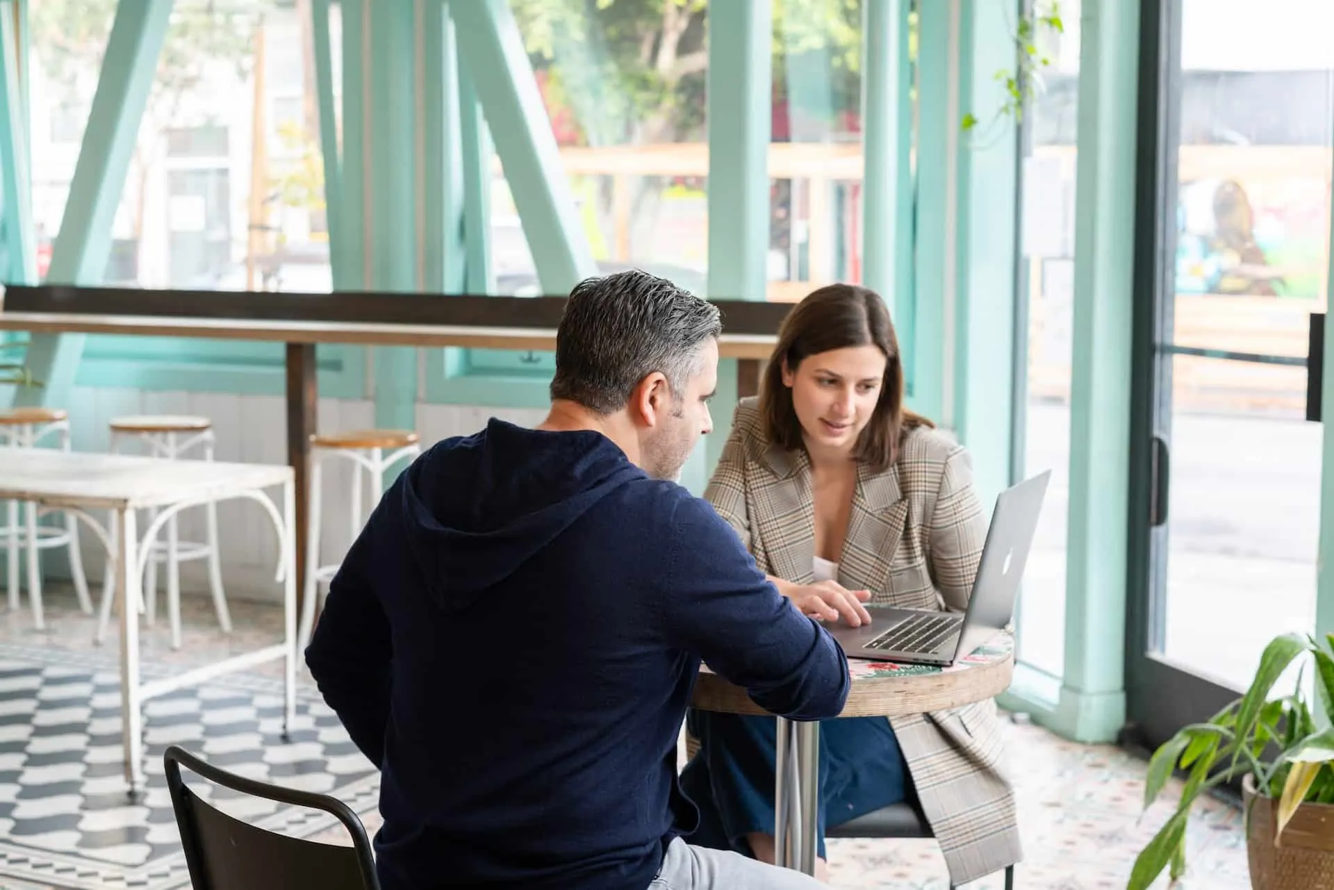 Un hombre y una mujer revisan un computador portátil en una mesa de un café.
