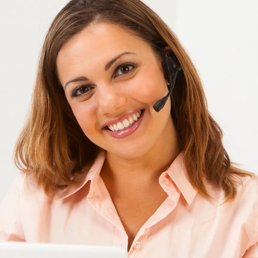 Mujer con audífono y micrófono, sonriendo frente a un computador.