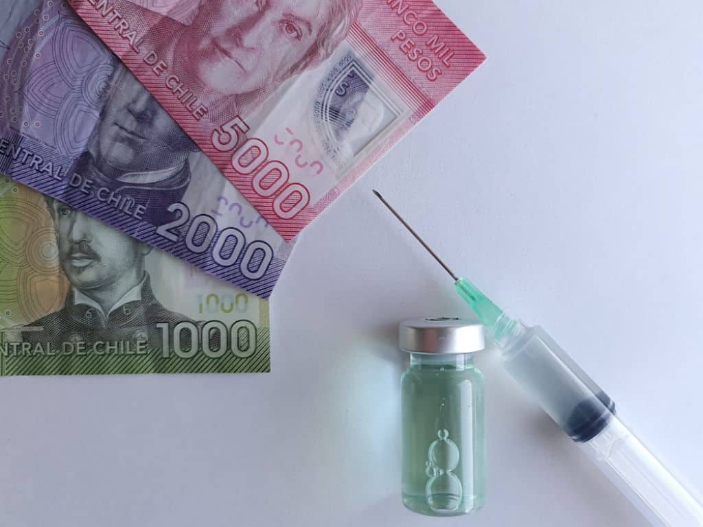 Imagen alegórica a la crisis de las Isapres, donde se muestra una serie de billetes de peso chileno sobre una mesa con una jeringa y una ampolla con solución médica para inyecciones.